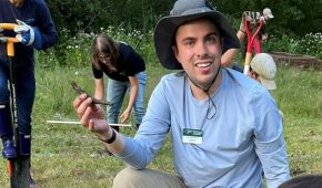 AmeriCorps volunteer sitting on ground smiling at camera with brick and second volunteer working on installing bricks